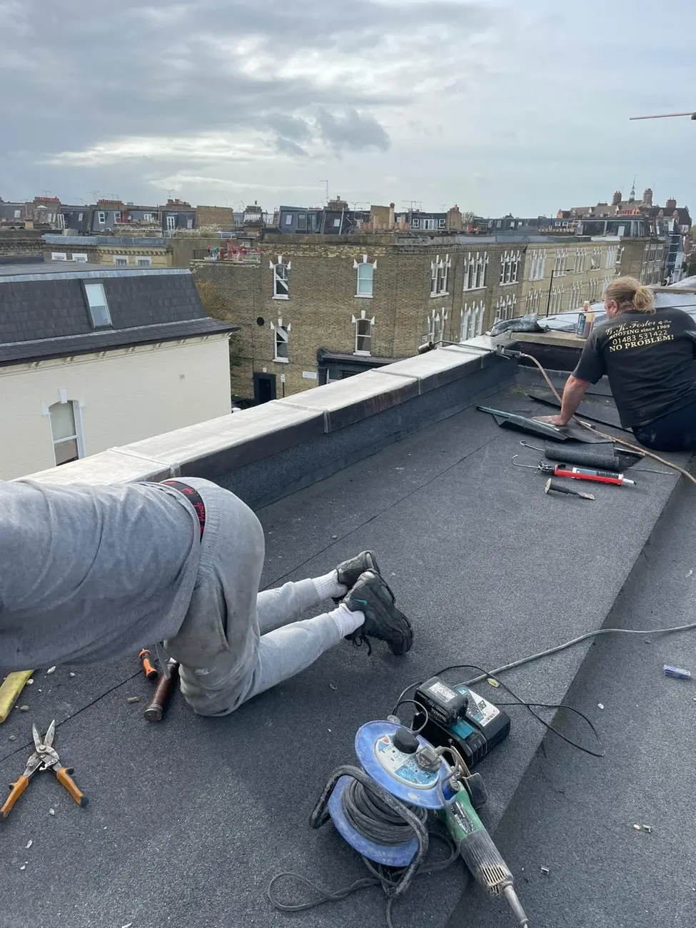 Two GK Foster & Son roofers bonding torch-on felt to a flat roof beside a lead-capped parapet