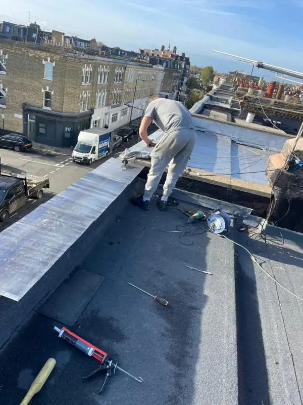 Roofer installing a torch-on felt flat roof covering with new lead edge detail